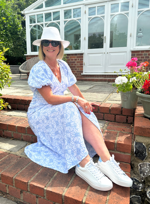 woman sat on brick steps wearing blue dress, white hat an white trainers from sans matin